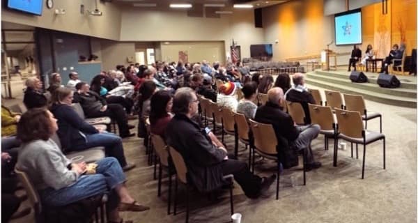 Community event with audience and stage with Interfaith Coalition branding