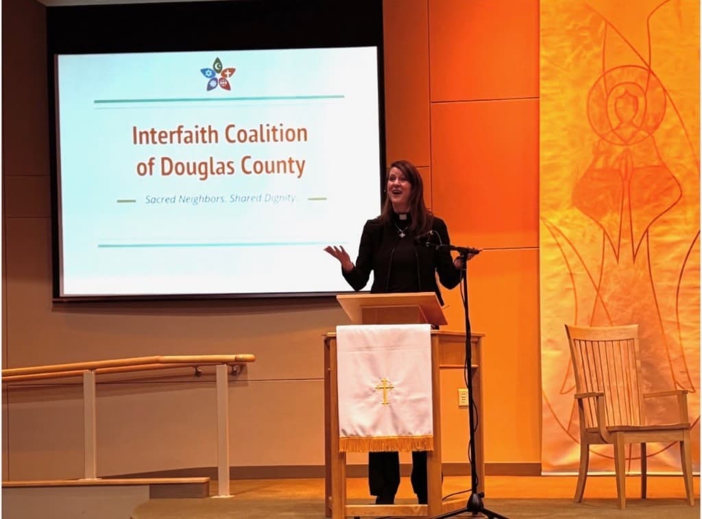 Speaker at podium with Interfaith Coalition of Douglas County slide